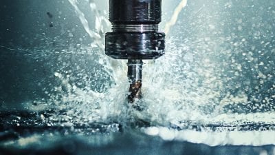 Closeup shot of a CNC machine processing a piece of metal. There are three water streams splashing the object to cool it down.